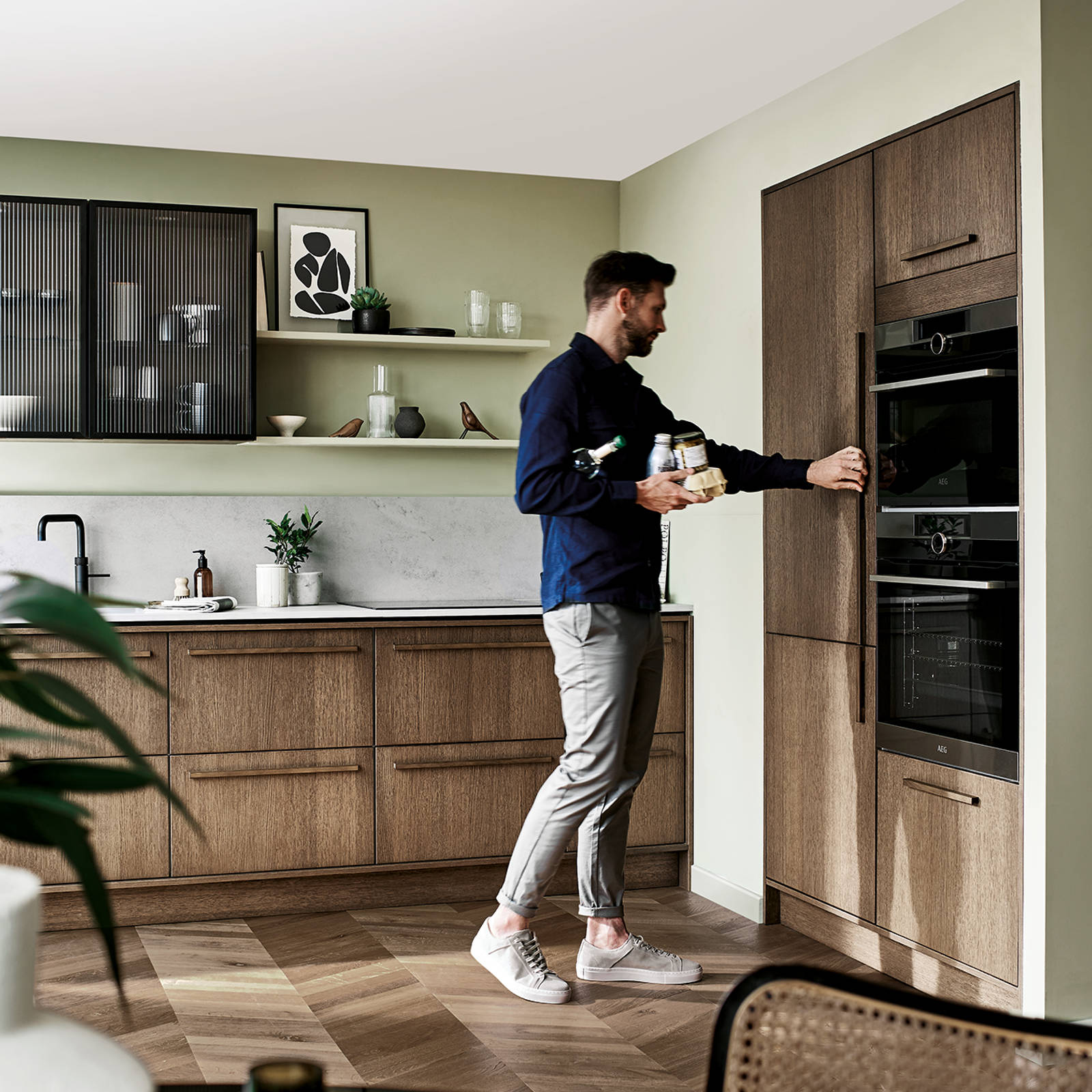 Man holding groceries in one hand opening the refrigerator with the other, in a Nordic oak kitchen from Magnet