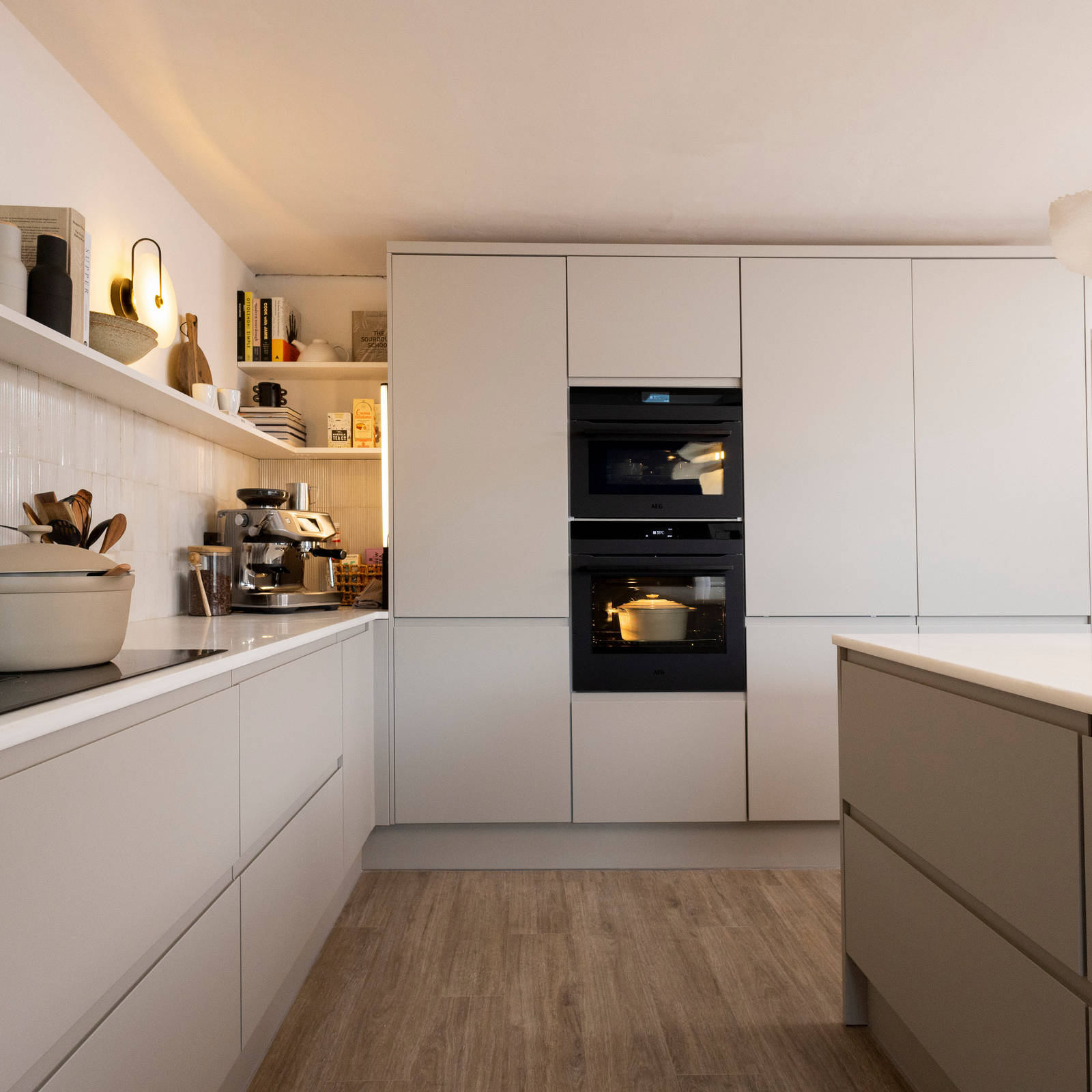 View of Yasmin Wyatt's open, light and airy neutral shade handleless Luna kitchen from Magnet, a white Corian worktop in Onyx, two AEG ovens integrated into tall cabinets.