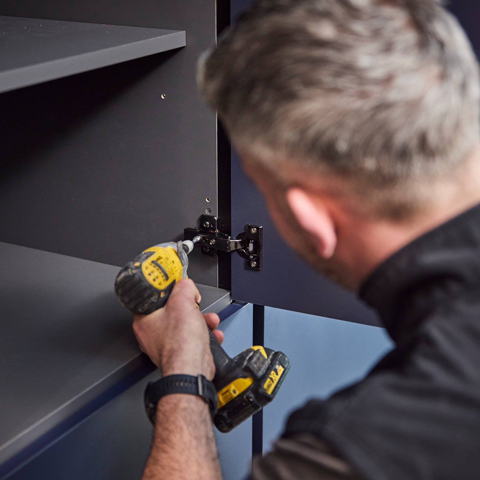 A tradesperson drilling hinges onto a cabinet