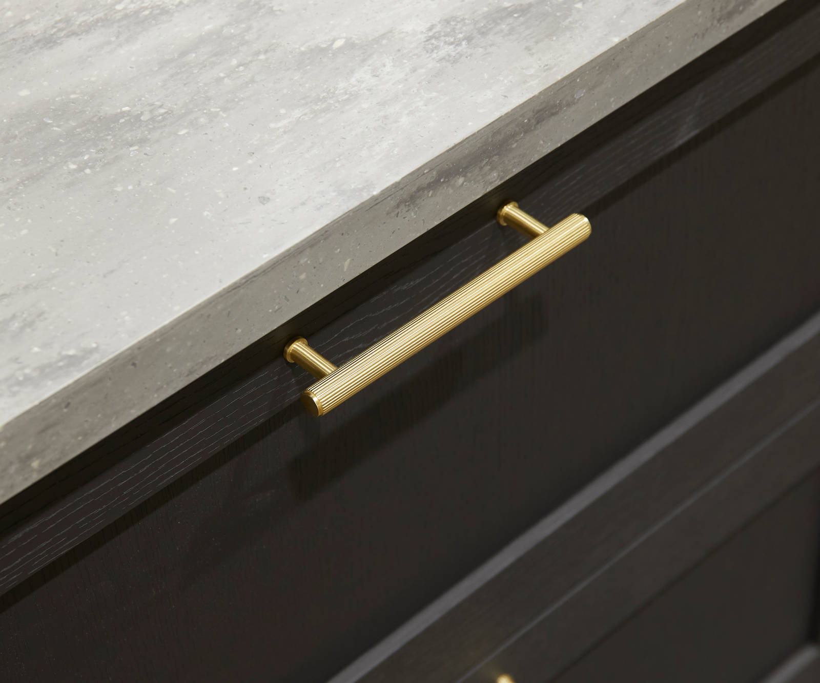 A close-up view of Ambleside drawer frontals in Graphite, with brass bar handles and grey worktop.