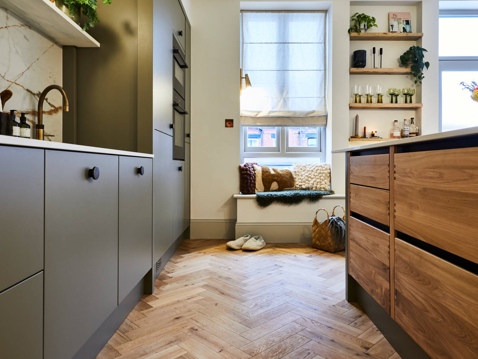 Parallell view of Nordic Craft kitchen island and modern slab Soho cabinets in the Balmoral colour, a soft beige green tone, as well as a seating area with pillows in earth tones.