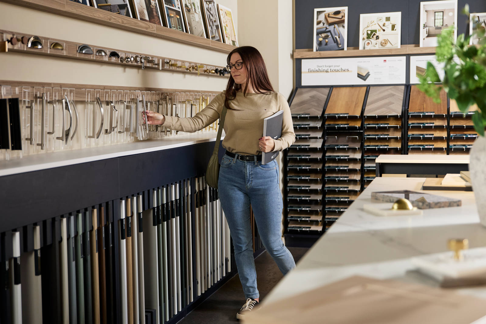 Woman reaching for sample handle at a Magnet showroom, along with samples of flooring, handles and other accessories.