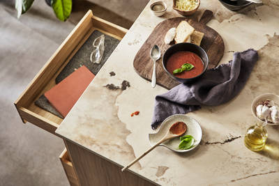 Bird view of kitchen island with Dekton Khalo Worktop, ceramic bowls containing tomato soup, bread and olive oil while an oak drawer is opened.