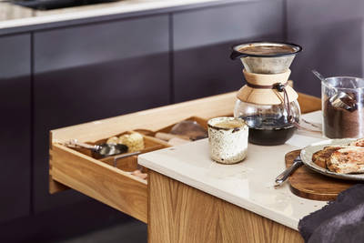 Close-up of opened oak drawer in Nordic Craft kitchen island, with breakfast served on handmade ceramics on the worktop.