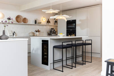 Diagnonal view of kitchen island corner in Yasmin Wyatt's open, light and airy neutral shade handleless Luna kitchen from Magnet with a white Corian worktop in Onyx, two AEG ovens integrated into tall cabinet and a wine cooler integrated into kitchen island.