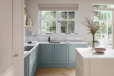 Open floor plan kitchen in light room, with blue Duck egg cabinetry as well as light beige Limestone shade kitchen island and tall cabinetry, matched with stel knobs and windows above sink area.