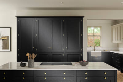 View over kitchen island in Traditional Shaker-style tactile woodgrain Ludlow Sumi Black kitchen with tall cabinets, brass accessories, marbled white and grey worktop, white ceramic sink and brass tap.