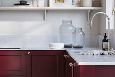 Wardley Morello kitchen cabinetry with steel knobs, steel tap, white marbled worktop and matching backsplash. An open shelf on the wall above cabinets with ceramics and a vase of flowers.